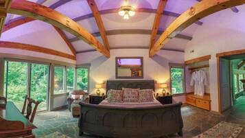 A spacious bedroom with a large bed, a stone floor, and a view of the outdoors through large windows.