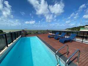 A rooftop pool with blue lounge chairs and a view of the ocean. - Torres e Cruz Serviços de Hospedagens Ltda (João Pessoa)