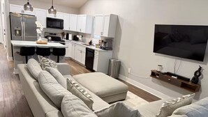 Un salon moderne avec un canapé, un téléviseur et une cuisine en arrière-plan.