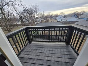 A wooden deck with a black railing, surrounded by trees and houses in the background.