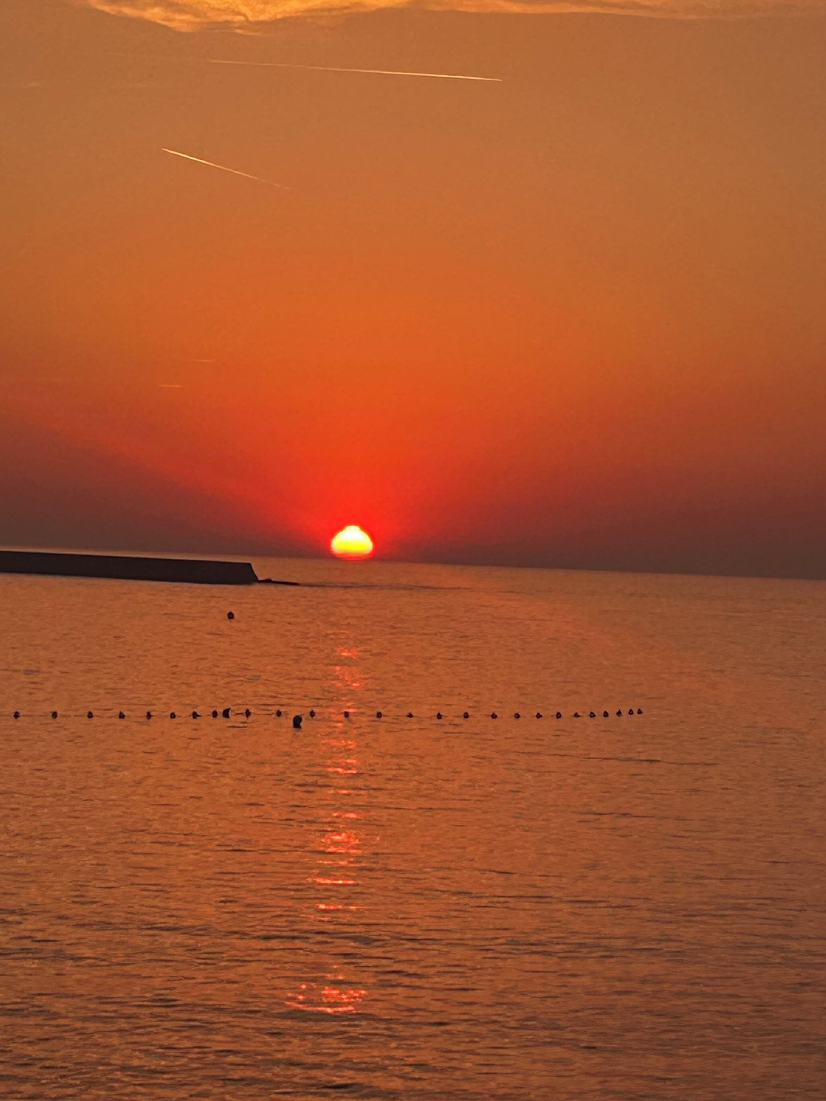 Un atardecer sobre un mar tranquilo con un muelle que se adentra en el agua.