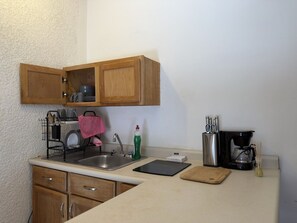 A compact kitchen with wooden cabinets, a sink, a coffee maker, and a tablet on the counter. - Mini loft junto a la UDEM (San Pedro Garza García)