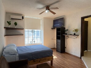 A bedroom with a bed, a ceiling fan, an air conditioner, a TV, and a window with a view. - Mini loft junto a la UDEM (San Pedro Garza García)