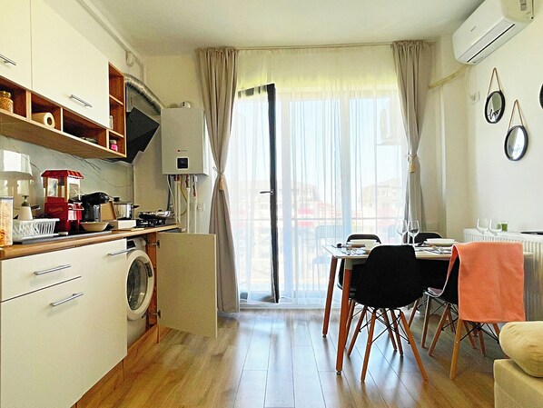 A compact kitchen with a washing machine, dining table with chairs, and a view through a large window. - Chic Studio+ FullKitchen+ Free Parking+ Popcorn (Chiajna)