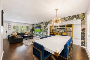 A modern kitchen with a central island, a dining area with blue upholstered chairs, and a living room with a sofa and coffee table. - Villa Banana | Heated Pool | Pool Table | PuttPutt (Wilton Manors)
