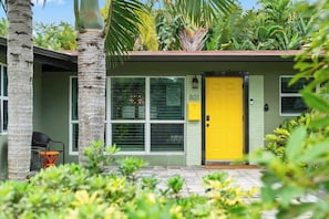 A small building with a yellow door, windows, and a small porch area with chairs. - Villa Banana | Heated Pool | Pool Table | PuttPutt (Wilton Manors)