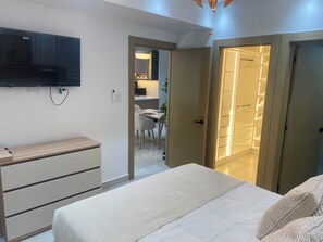 Ein Schlafzimmer mit einem Bett, einem an der Wand montierten Fernseher, einer Holzkommode und einer Tür zu einem Badezimmer.
