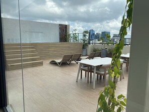 Eine Dachterrasse mit Holzboden, Liegestühlen, einem Esstisch und Topfpflanzen.