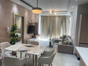 Ein modernes Wohnzimmer mit Essbereich, einem Flachbildfernseher, einem Deckenventilator und einem großen Fenster mit Vorhängen.