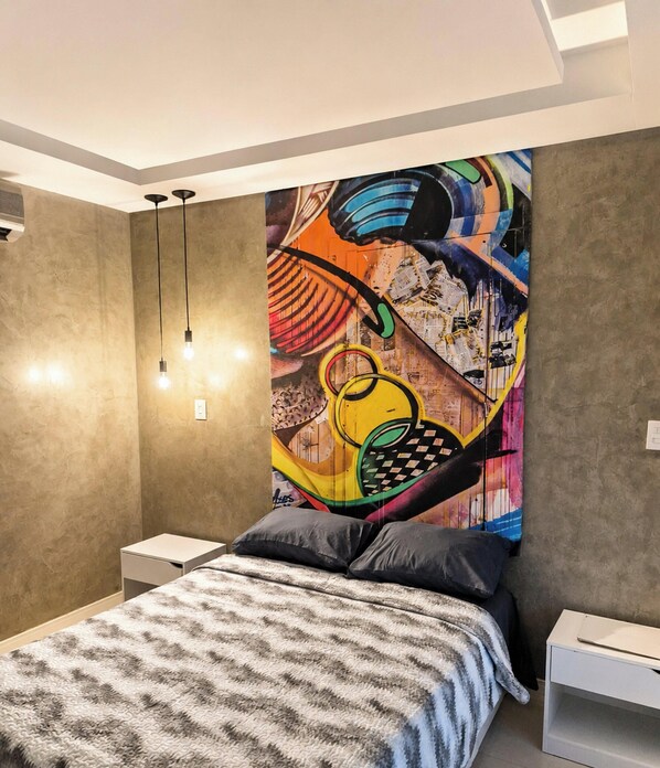 A modern bedroom with a large bed, bedside tables, and a colorful abstract painting on the wall. - Studio no Coração da Cidade Velha - PA (Belém)