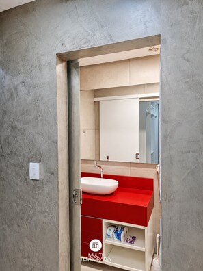A bathroom with a white sink, red countertop, and a mirror above it.