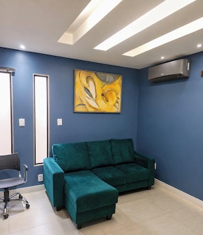A room with a teal sofa, a painting on the wall, and a ceiling light fixture.