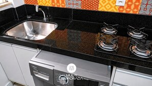Cozinha com pia de aço inoxidável, bancada preta e fogão a gás com três bocas.