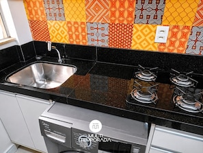 A kitchen with a stainless steel sink, black countertop, and a gas stove.