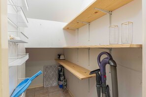 Quarto com paredes brancas, teto de madeira e estantes com diversos objetos.