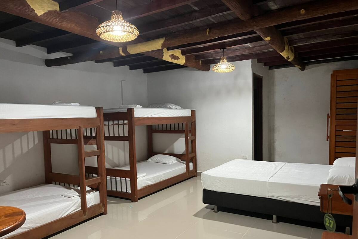 A room with bunk beds, a single bed, a wooden table, and a hanging light fixture.