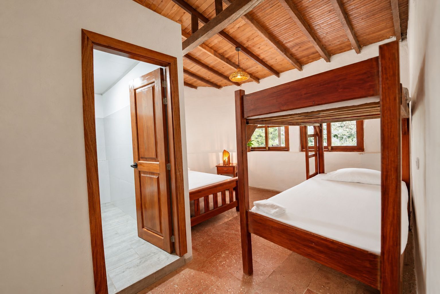 A bedroom with two wooden beds, a nightstand, a lamp, and a window with a view.