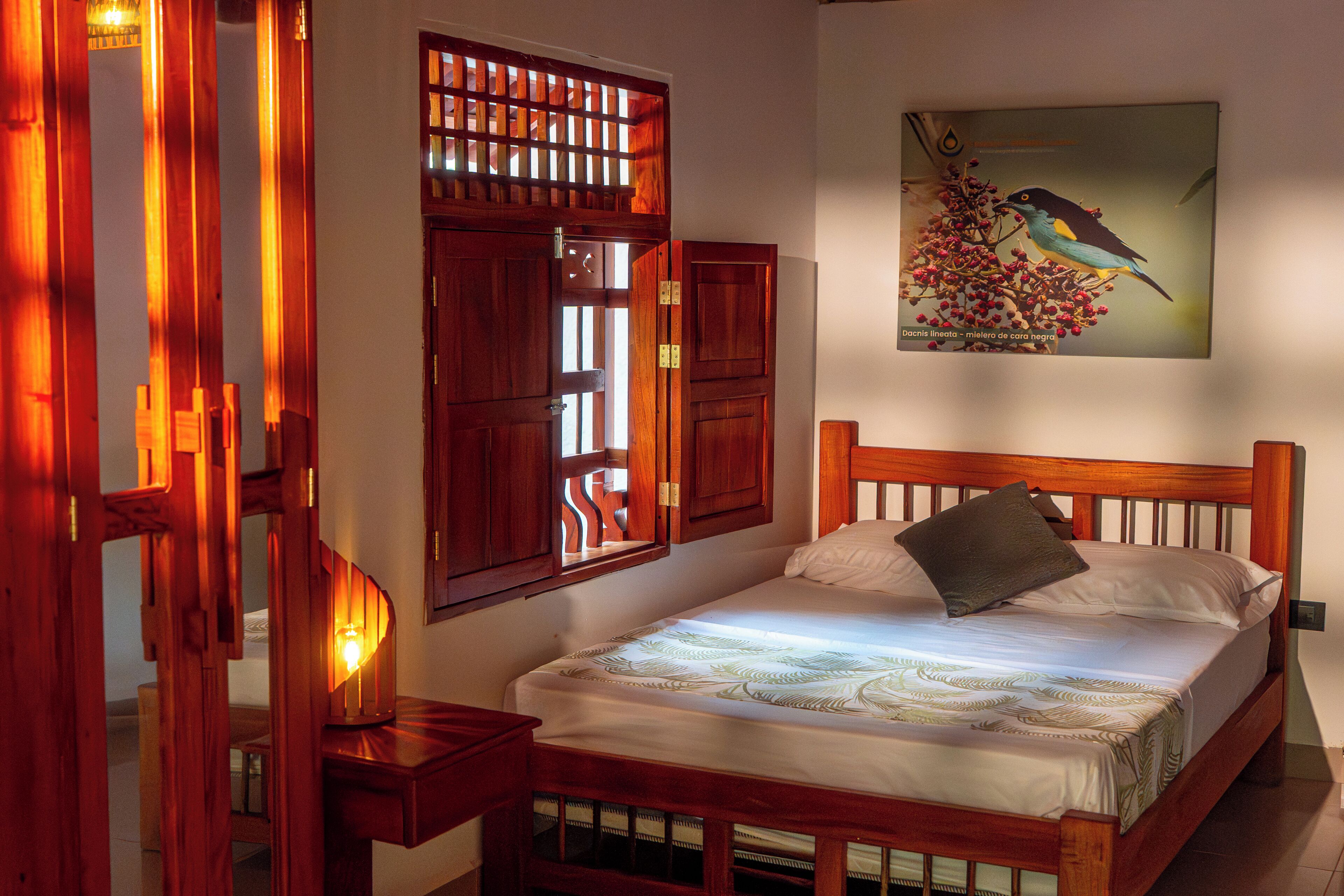 Un dormitorio con cama de madera, mesita de noche, un cuadro en la pared y una ventana con contraventanas de madera.