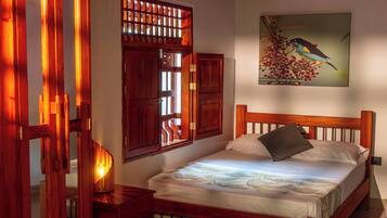 Un dormitorio con cama de madera, mesita de noche, un cuadro en la pared y una ventana con contraventanas de madera.