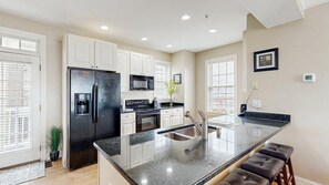 A modern kitchen with white cabinets, a black refrigerator, a microwave, and a sink. - Spacious coastal townhouse with multiple decks, gas fireplace, & relaxing Bay views (Ocean City)