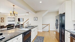 A modern kitchen with a central island, stainless steel appliances, and a staircase leading to an upper level. - Spacious coastal townhouse with multiple decks, gas fireplace, & relaxing Bay views (Ocean City)
