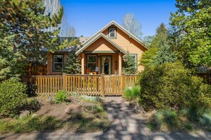 A single-story house with a porch, surrounded by a wooden fence and dense greenery. - Bluebird Day - Desert Zen in Bend with 2 queens, fenced yard, fireplace, Walk Everywhere! (Bend)