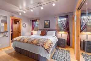 A bedroom with a large bed, bedside tables, a wardrobe, and a window with curtains. - Bluebird Day - Desert Zen in Bend with 2 queens, fenced yard, fireplace, Walk Everywhere! (Bend)