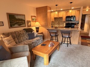 Ein Wohnzimmer mit einer Couch, einem Couchtisch und einer Küchenzeile mit einer Bar und Hockern.