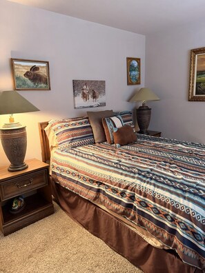 Ein Schlafzimmer mit einem Bett, zwei Nachttischen, einer Lampe und Wandbildern.