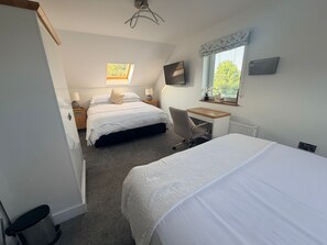 A bedroom with two beds, a desk, a chair, a TV, and a window with a view of greenery. - Ardbrin Lodge Guest Accommodation  (Antrim)