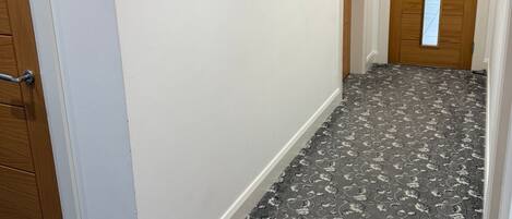 A hallway with a patterned carpet, a wooden door, and a mirror on the wall.