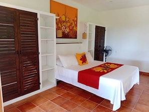 A bedroom with a bed, a wardrobe, a fan, and a wall painting. - Heiva - Fare Orotia (Avera, Raiatea)
