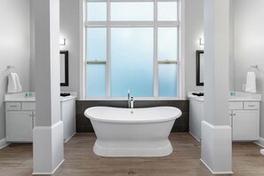 Une salle de bain moderne avec une baignoire sur pieds, des meubles blancs et une grande fenêtre offrant une vue dégagée.