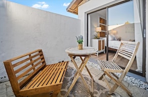 A wooden bench and table set on a patio with a view of a bedroom through a glass door. - KoKo Hut Golf Views Fenced Coastal Cottage (Palm Coast)