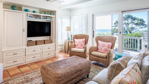 A living room with a television, wicker furniture, and a view of the sea.