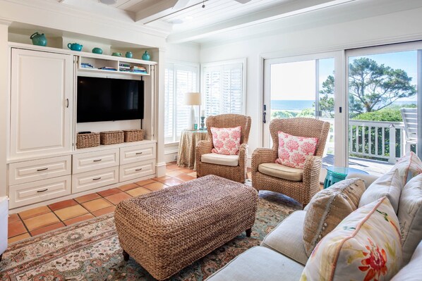 A living room with a television, wicker furniture, and a view of the sea. - Luxury Oceanfront Villa w/ Stunning Ocean Views, Balconies, Boardwalk Beach Access & Community Pool (Kiawah Island)