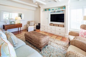A living room with a sofa, ottoman, TV, and storage unit. - Luxury Oceanfront Villa w/ Stunning Ocean Views, Balconies, Boardwalk Beach Access & Community Pool (Kiawah Island)
