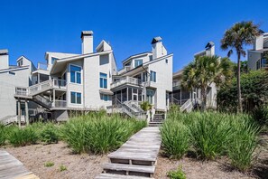 A coastal residential area with multiple houses, a wooden pathway, and palm trees. - Luxury Oceanfront Villa w/ Stunning Ocean Views, Balconies, Boardwalk Beach Access & Community Pool (Kiawah Island)