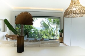 Ein modernes Zimmer mit großem Fenster, einem weißen Sofa, einer hölzernen Vase mit Pflanze und einer gewobenen Leuchte.
