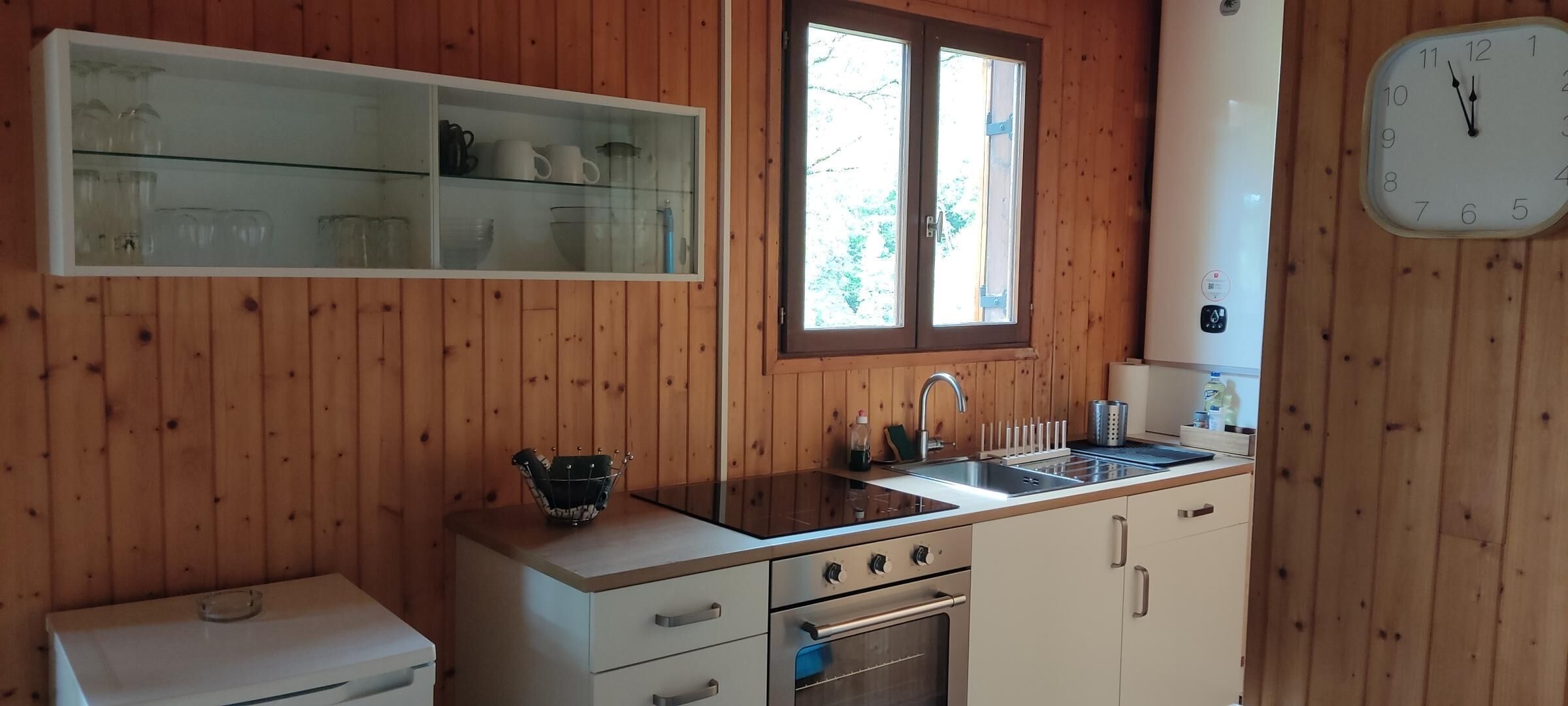 Cocina compacta con paredes de madera, estante empotrado, pileta, estufa y un reloj.