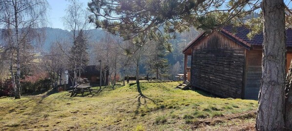 Un chalet rustique aux murs en bois, entour é d’une zone herbeuse avec des arbres et une table de pique-nique.