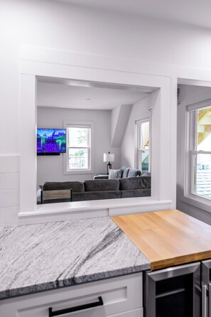 Eine moderne Küche mit Marmorarbeitsplatte, einem eingebauten Holzesstisch und einer Sitzecke inklusive Sofa und Fernseher.