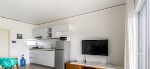 Eine moderne Küche mit weißen Schränken, einer Mikrowelle, einem Kühlschrank und einem flachbildfernseher an der Wand.