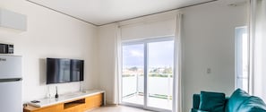 Eine moderne Wohnung mit Küche, Flachbildfernseher, einem blaugrünen Sofa und einem Balkon mit Blick.