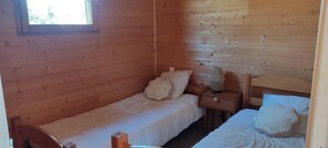 A wooden cabin room with two beds, a nightstand, a lamp, and a window. - Chalet Brumalis - MALZIEU VILLE (LE) (MALZIEU VILLE (LE))