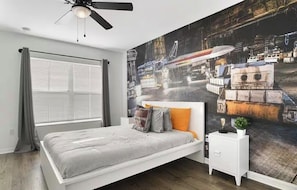 Ein Schlafzimmer mit einem Bett, Deckenventilator, einem Fenster mit Vorhängen und Wandgemälde.