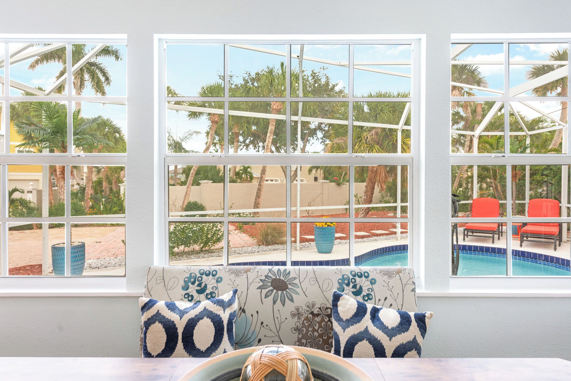 Une chambre avec vue sur une piscine, un espace salon extérieur et une fenêtre donnant sur des palmiers.