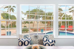 Habitación con vistas a una piscina, mobiliario exterior y ventana con vista a palmeras.