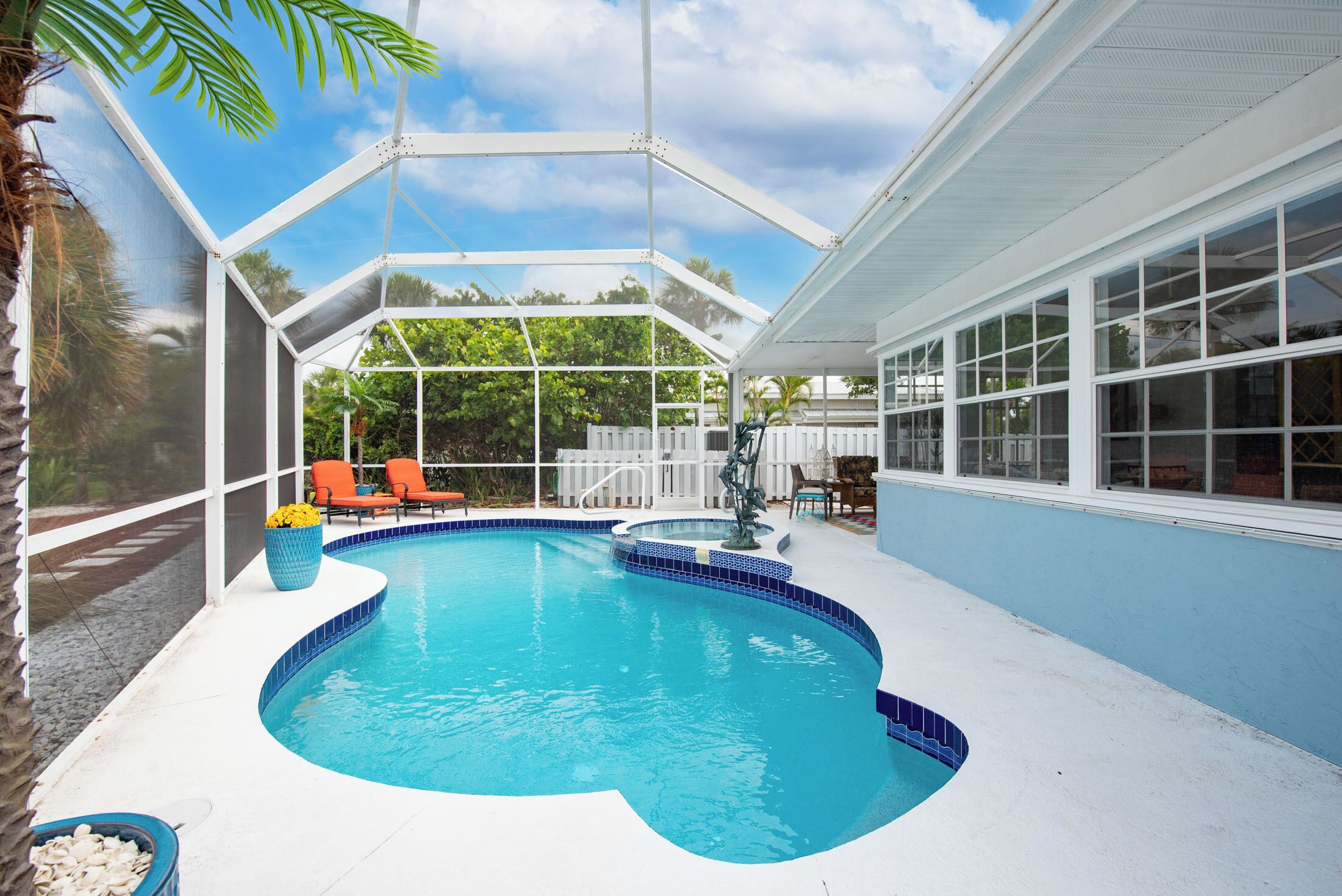 Une piscine à bord incurvé, entourée d’une terrasse blanche et protégée par une enceinte en verre.