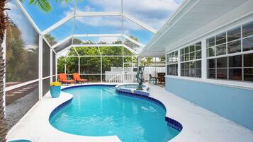 Une piscine à bord incurvé, entourée d’une terrasse blanche et protégée par une enceinte en verre.